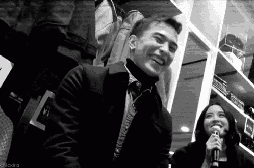 a black and white photo of a man laughing and a woman speaking into a microphone