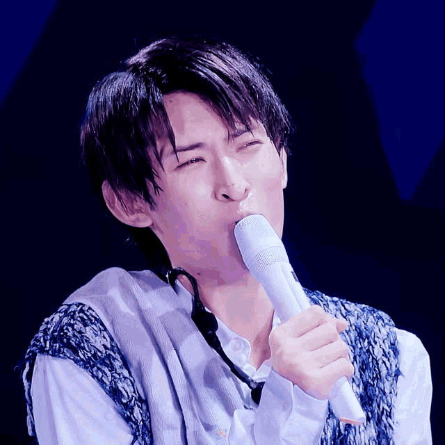 a young man singing into a white microphone with his eyes closed