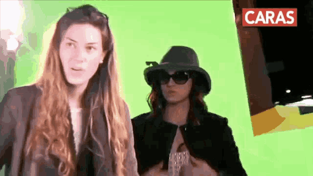 two women standing next to each other in front of a green screen with the word caras on it