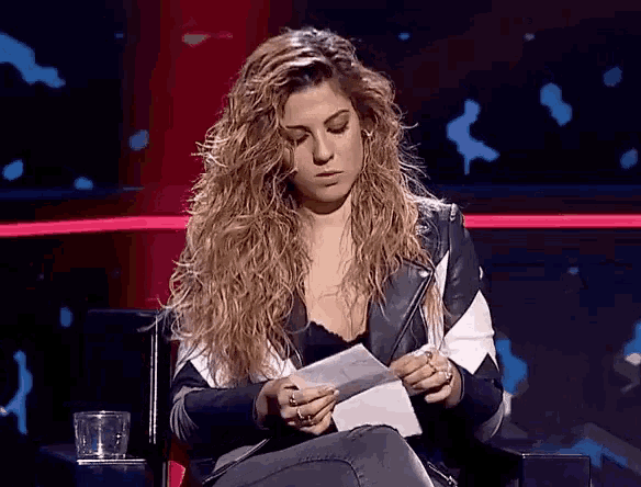 a woman with long curly hair is sitting in a chair holding a piece of paper