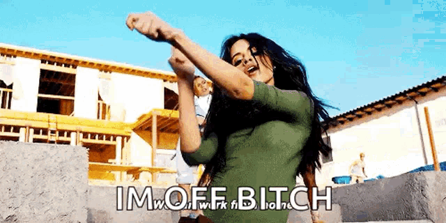 a woman in a green dress is dancing in front of a building under construction and the words im off bitch are above her
