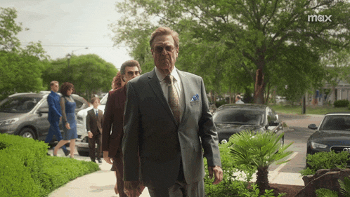a man in a suit and tie walks down a sidewalk with a max logo in the background