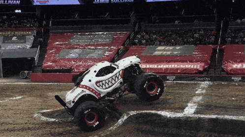 a monster truck is driving down a dirt track in a stadium