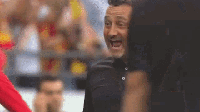 a man with a beard is standing in front of a crowd and yelling .