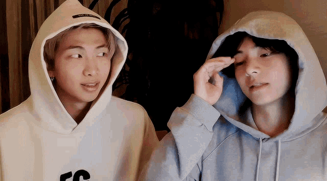 two men wearing hoodies are standing next to each other in a room .
