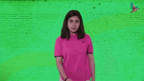 a woman in a pink shirt stands in front of a green wall with the words eyes on the good times written on it .