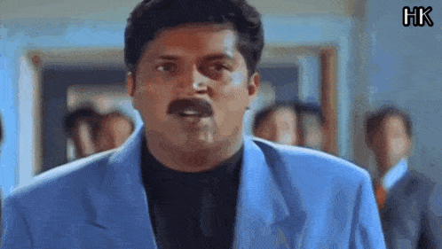 a man in a blue suit and black shirt is making a funny face .