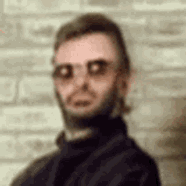 a man with a mullet and glasses is standing in front of a brick wall and looking at the camera .