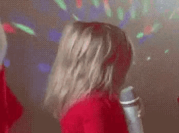 a woman in a red shirt is holding a microphone and dancing in a dark room .