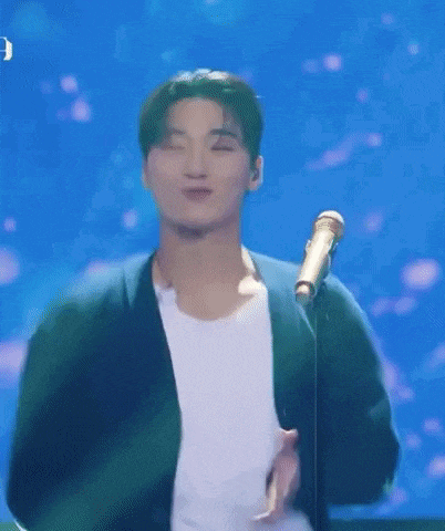 a man is standing in front of a microphone on a stage and singing into it .