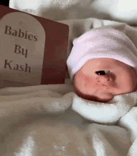 a baby wearing a pink hat is laying next to a book titled babies by kash