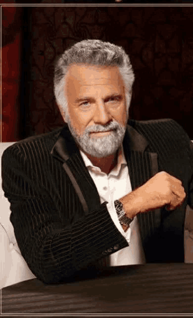 a man with a beard and a tuxedo is sitting at a table with his arm crossed .
