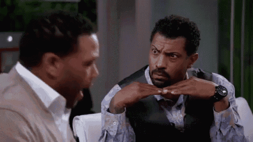 two men are sitting on a couch talking to each other and one of them is making a face .