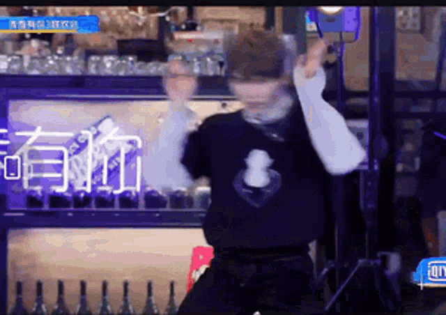 a man wearing a black shirt with a heart on it is dancing in front of a bar .