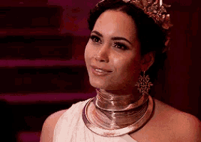 a woman in a white dress and gold jewelry is wearing a crown and earrings .
