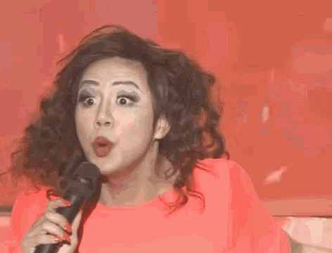 a woman with curly hair is holding a microphone in her hand and making a funny face .