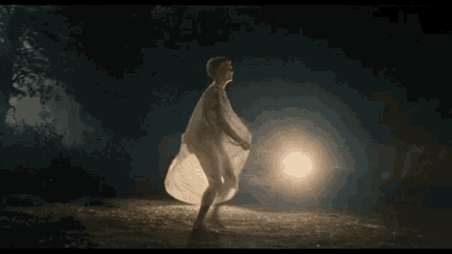 a woman in a white dress is standing in a dark area