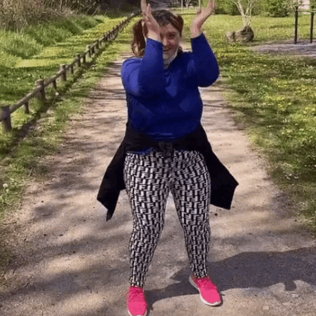 a woman wearing a blue shirt and pink shoes is dancing on a dirt road