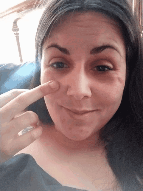 a woman is pointing at her face with her finger and smiling