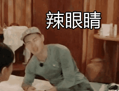 a man in a hat is sitting on a bed with chinese writing on the wall behind him .