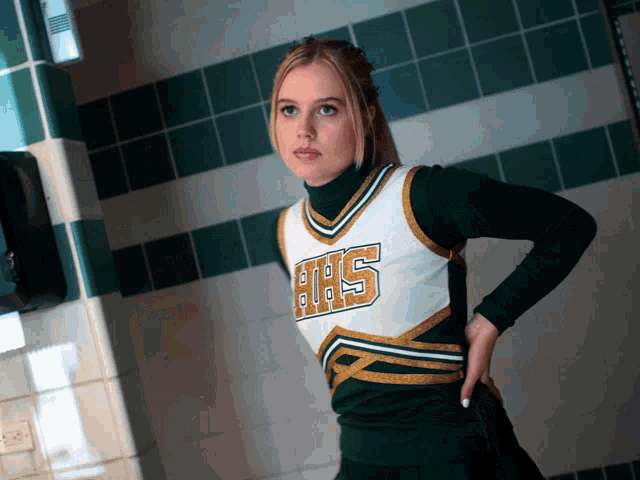 a cheerleader wearing a hhs uniform stands in a hallway