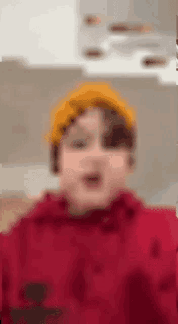 a young boy wearing a yellow hat and a red hoodie is making a funny face .