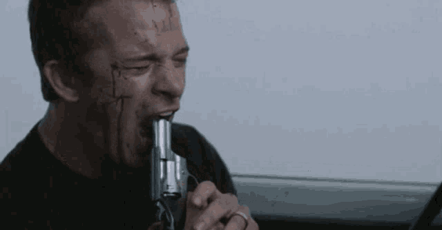 a man with blood on his face is biting a gun in his mouth .