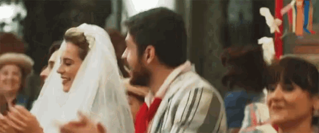 a bride and groom are sitting next to each other in a crowd of people at a wedding .