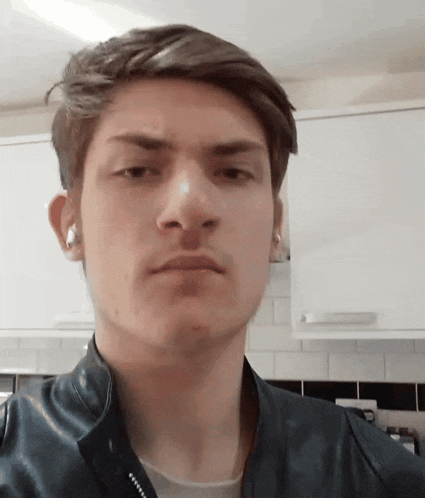 a young man wearing ear buds and a leather jacket looks at the camera