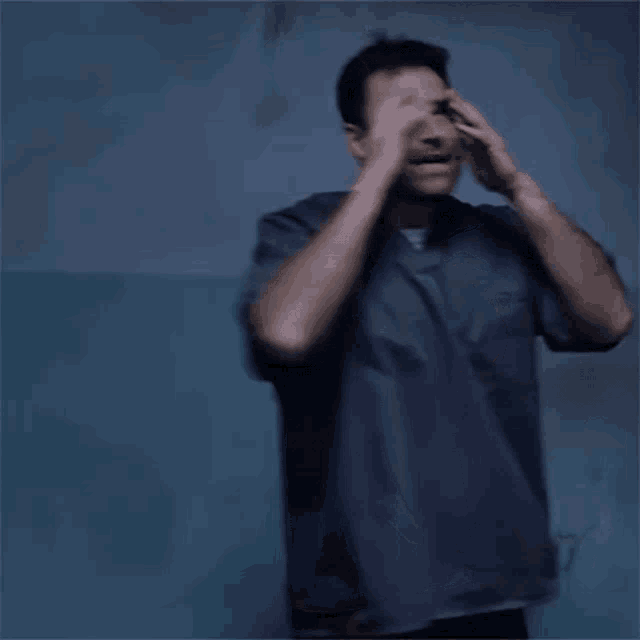 a man is covering his face with his hands in a dark room