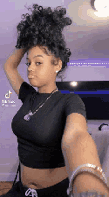 a woman in a black crop top is taking a selfie with her hair in a bun .