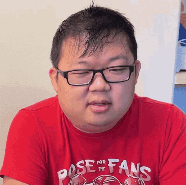 a man wearing glasses and a red pose for fans shirt