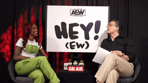 two women sit in front of a sign that says hey ew
