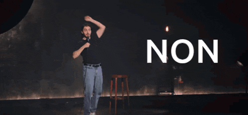 a man in a black shirt stands on a stage with the word non behind him