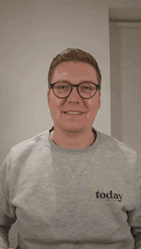 a man wearing glasses and a today sweatshirt holds a mug