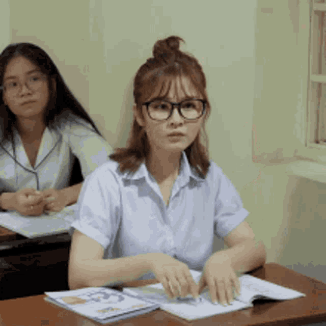 a girl with glasses sits at a desk in a classroom