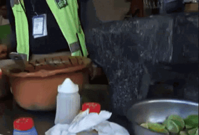 a man in a yellow vest is standing next to a bowl of food and bottles .