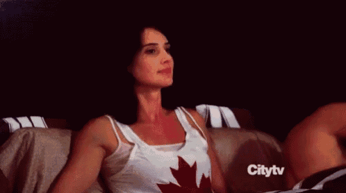 a woman is sitting on a couch wearing a tank top with a canadian flag on it