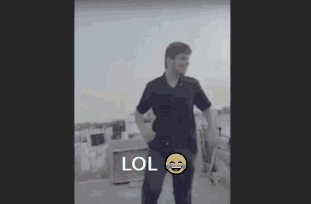 a man in a black shirt is standing with his hands in his pockets and a lol smiley face on his chest