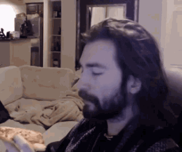 a man with long hair and a beard is sitting on a couch in a living room