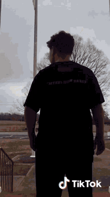 a man in a black shirt is standing in front of a flag pole with tiktok written on the bottom