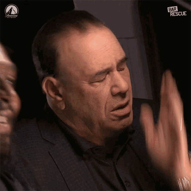 a man in a suit and black shirt is waving his hands in front of a paramount logo