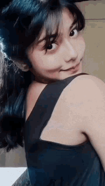 a young girl with blue hair is wearing a black tank top and smiling .