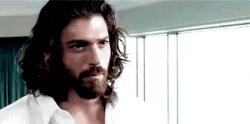 a man with long hair and a beard is wearing a white shirt and looking at the camera .