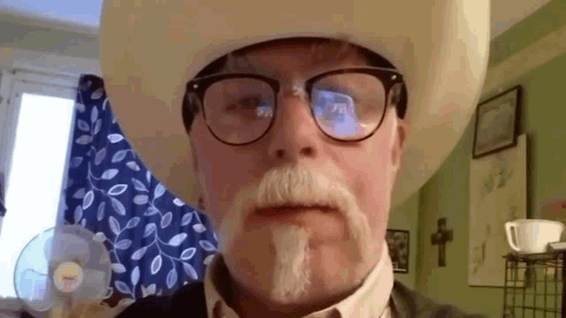 a man wearing a cowboy hat and glasses is looking at the camera .