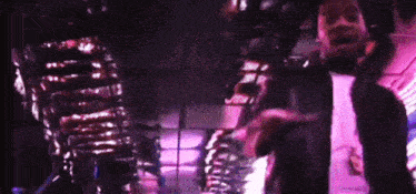 a man in a black jacket is standing in a dark room with a purple background