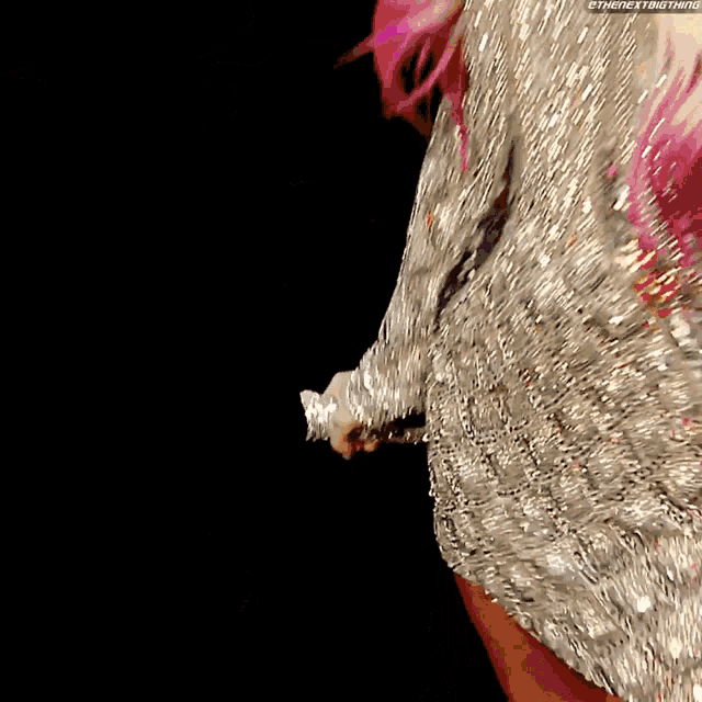 a woman with pink hair is wearing a silver dress and holding a microphone .