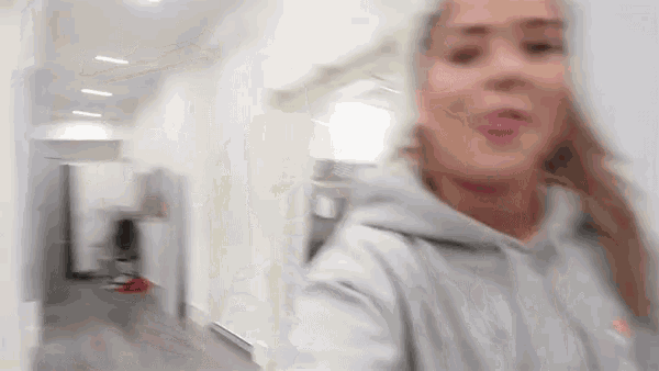 a blurry picture of a woman in a gray hoodie standing in a hallway .