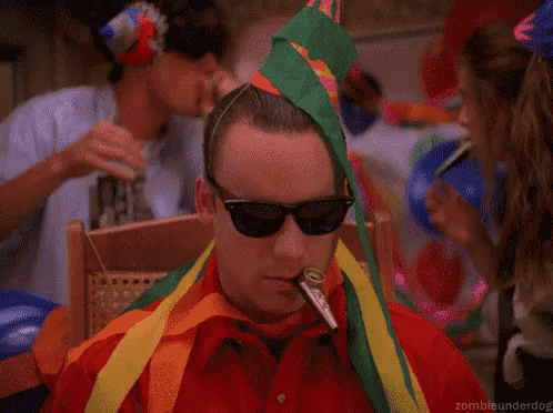 a man wearing sunglasses and a party hat is sitting in a chair .