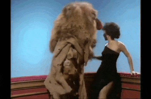 a woman in a black dress is standing next to a stuffed lion with a long mane .